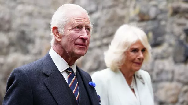 King Charles looking thoughtful with Queen Camilla stood beside him